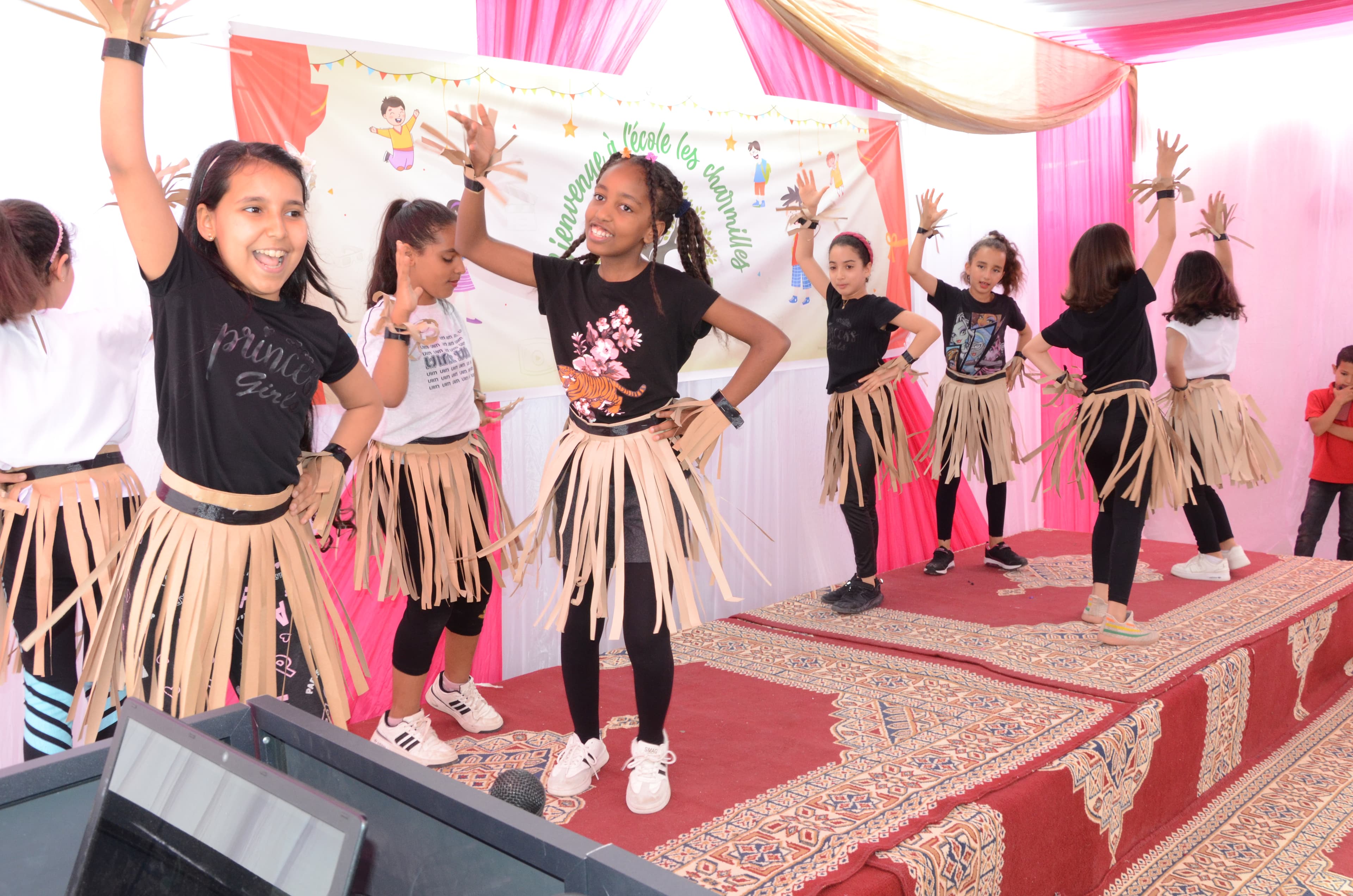 Filles en costumes avec des jupes de style paille exécutant une danse rythmée avec les bras levés lors du spectacle de l'école.