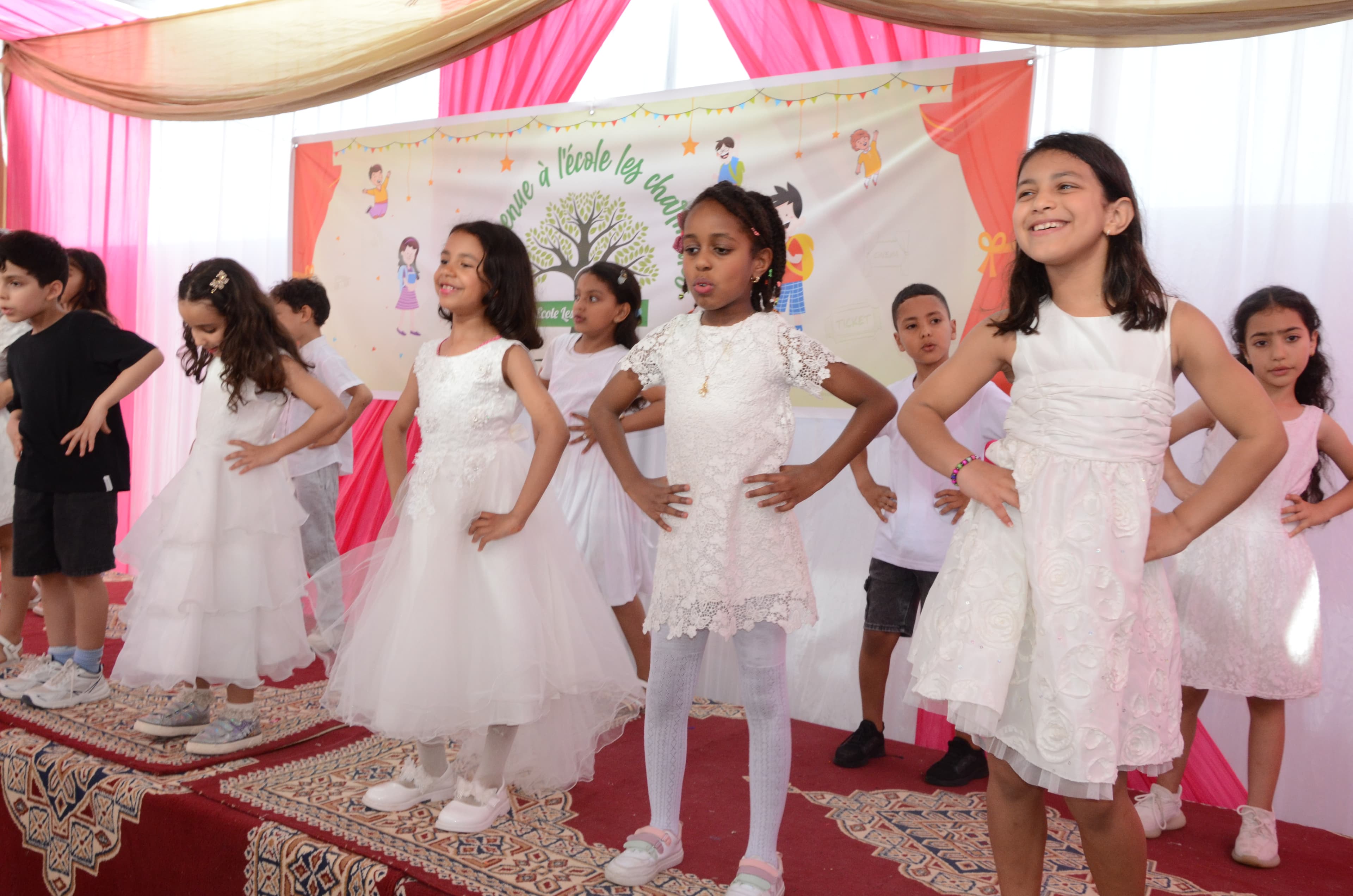 Groupe de filles vêtues de jolies robes blanches en pleine performance de danse sur la scène de l'école.