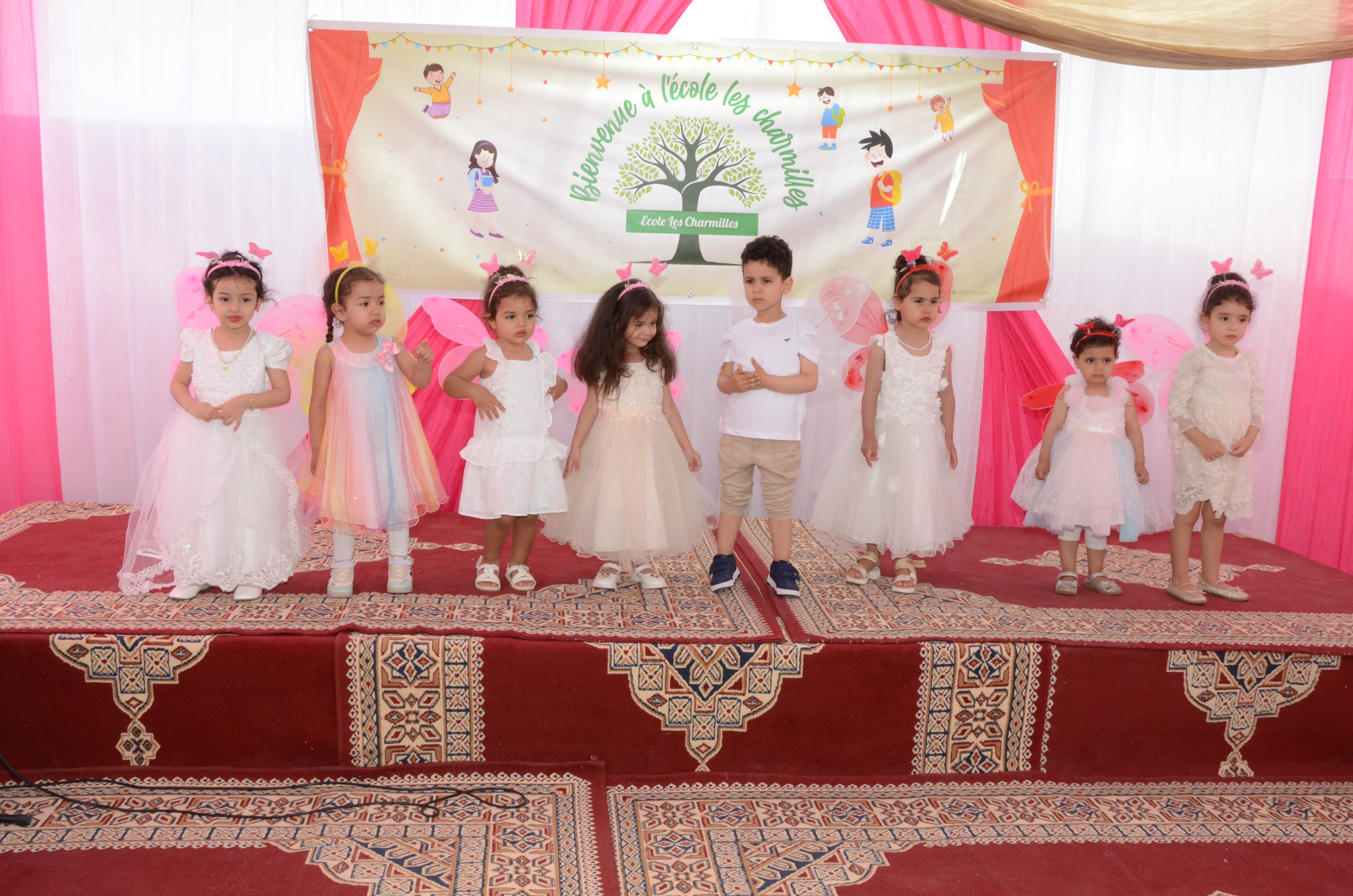 Très jeunes enfants, principalement des filles en robes de fête blanches et roses, posant timidement sur scène.